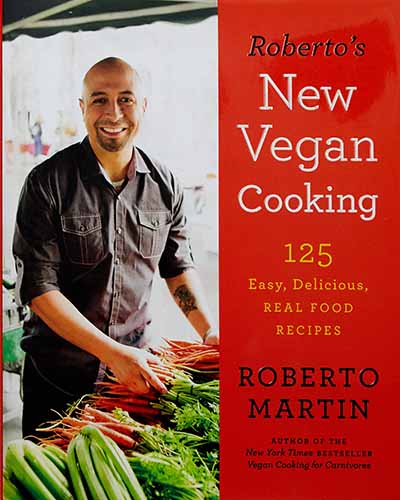 Cover for the book Roberto's New Vegan Cooking. Features a picture of the author, a man, shopping for carrots at a farmers market.