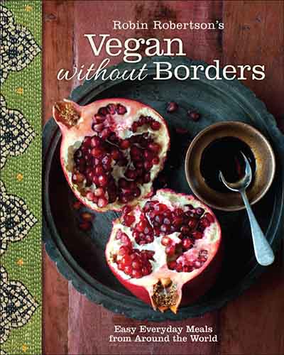 Cover for the book Vegan Without Borders. Features an overhead picture of a split pomegranate sitting on a black dish which is on top of a wooden surface.