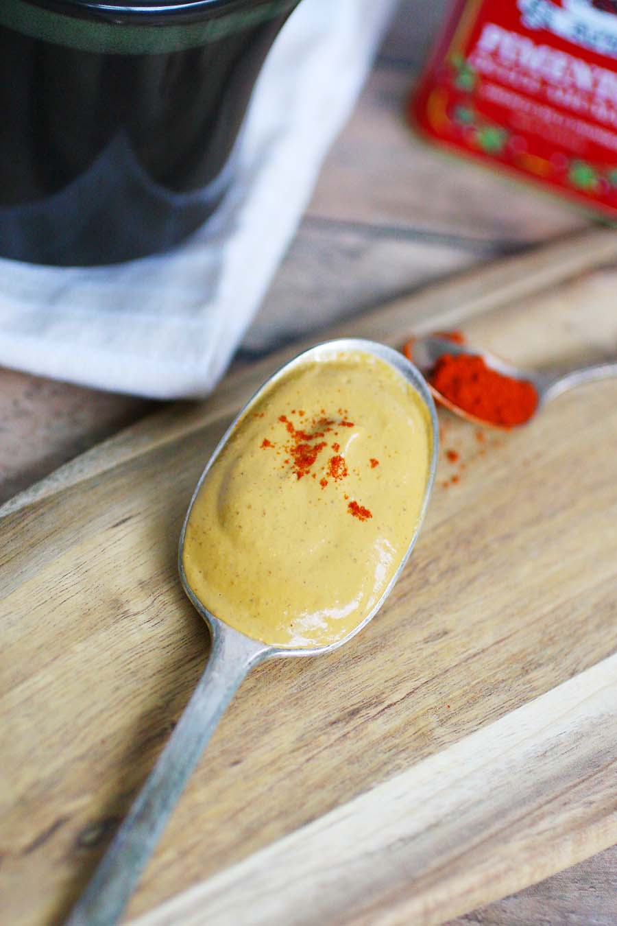 A spoon full of cream sitting on a wooden board with paprika dusted on top.