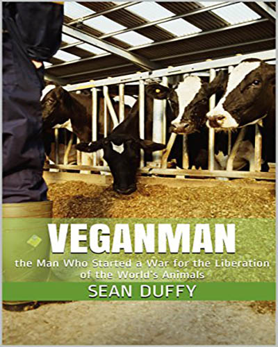 Cover for the book, Veganman. Features a picture of an industrial cow barn with cows eating hay while a pair of legs looks on.