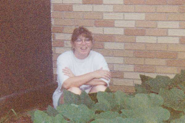 A young woman sitting among the bushes, smiling.