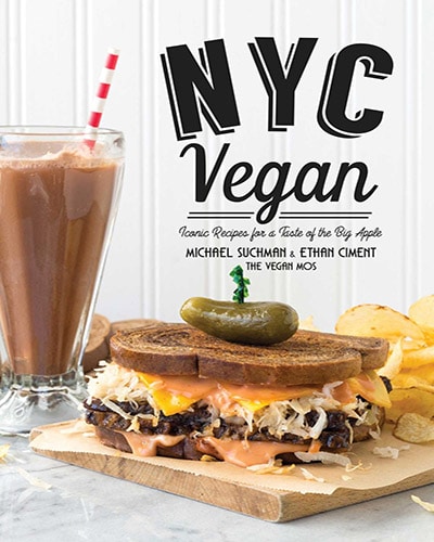 Cover for the book, NYC Vegan. Features a deli sandwich with potato chips sitting on top of a wooden board. In the background is a chocolate shake.