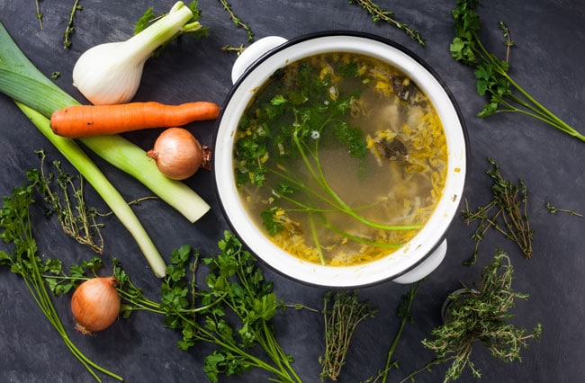 An overhead picture of a pot of vegetable stock with various whole vegetables surrounding the pot.