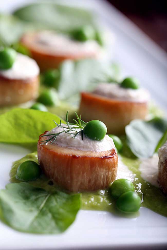 A closeup picture of vegan scallops and peas sitting on a white plate.