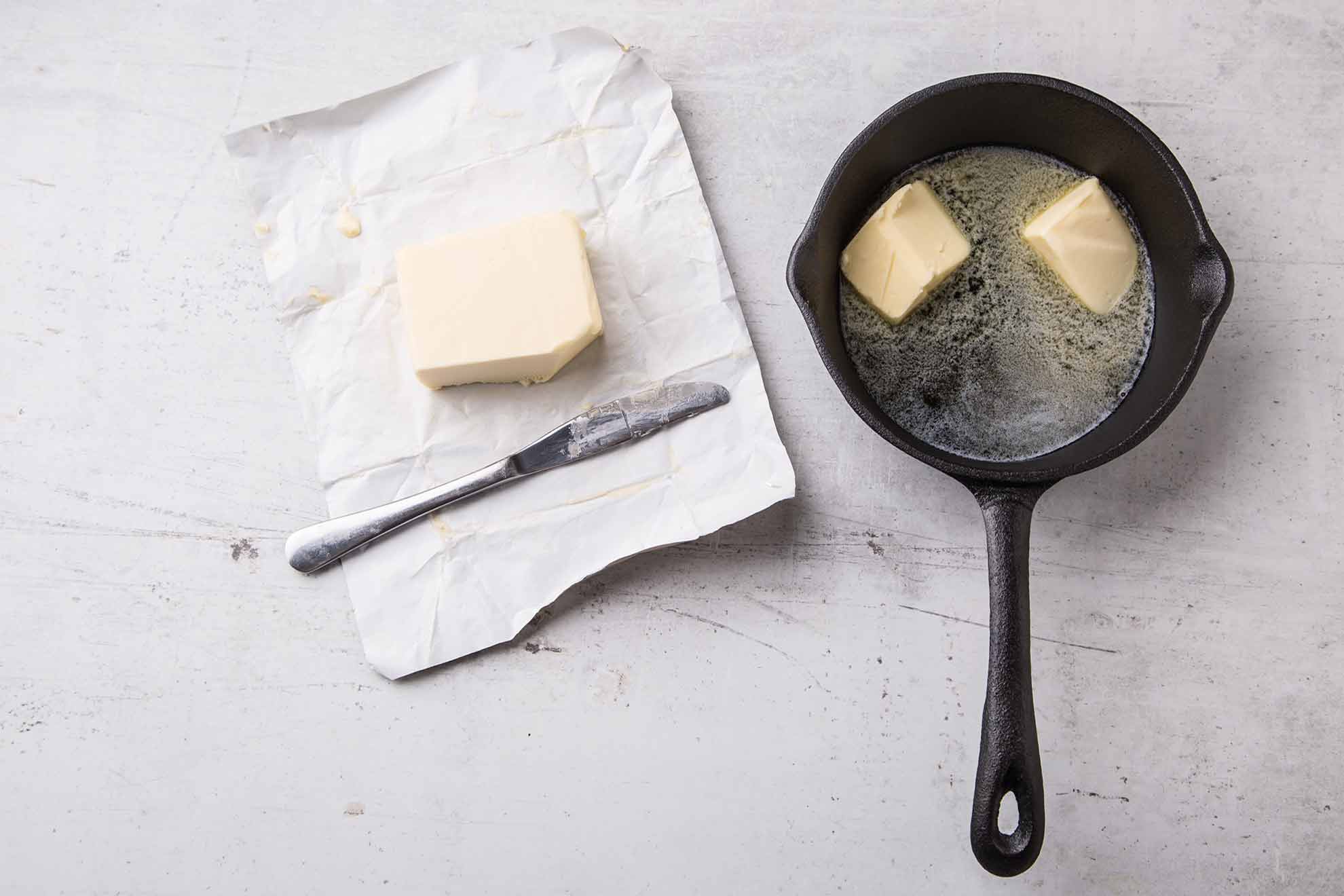 An iron skillet with melting butter sitting on a counter and next to an open package of margarine.