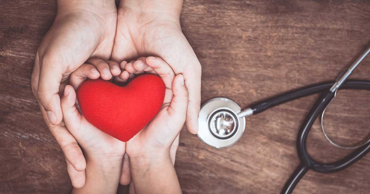 Two hands holding a heart next to a stethoscope