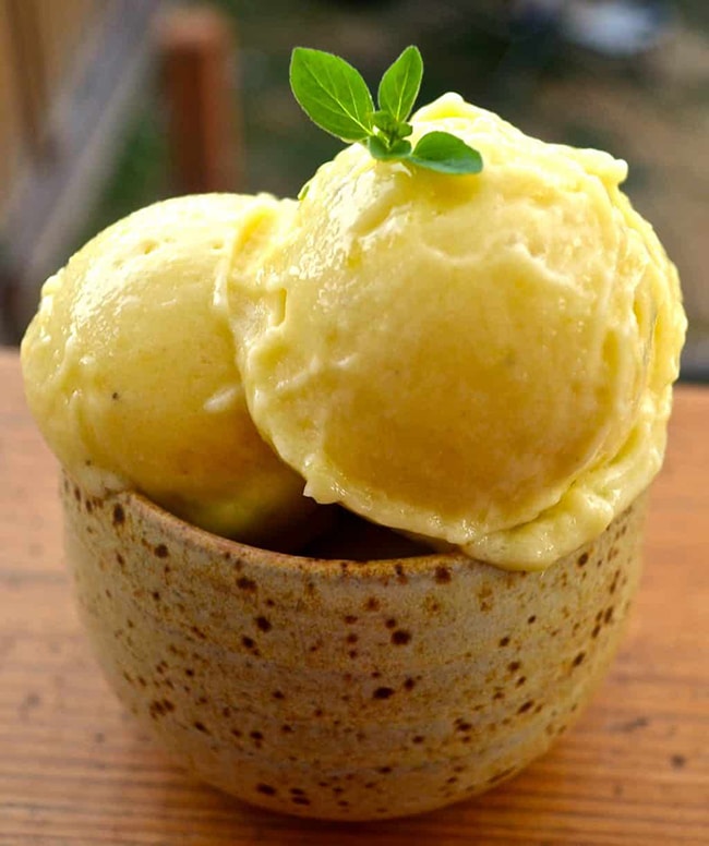 Two scoops of a vegan mango ice cream in a stonewear bowl with a fresh sprig of mint on top.