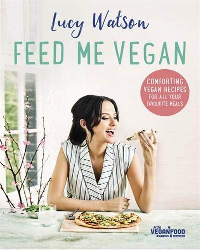 Cover for the book, Feed Me Vegan. Features a picture of the author, a woman, sitting at a white table and eating a piece of pizza.