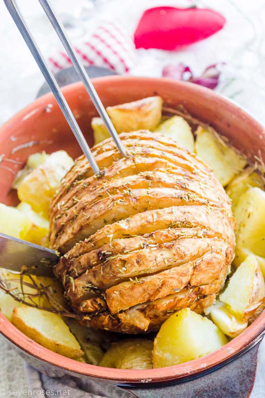 A holiday roast sitting in a casserole dish surrounded with roasted potatoes.