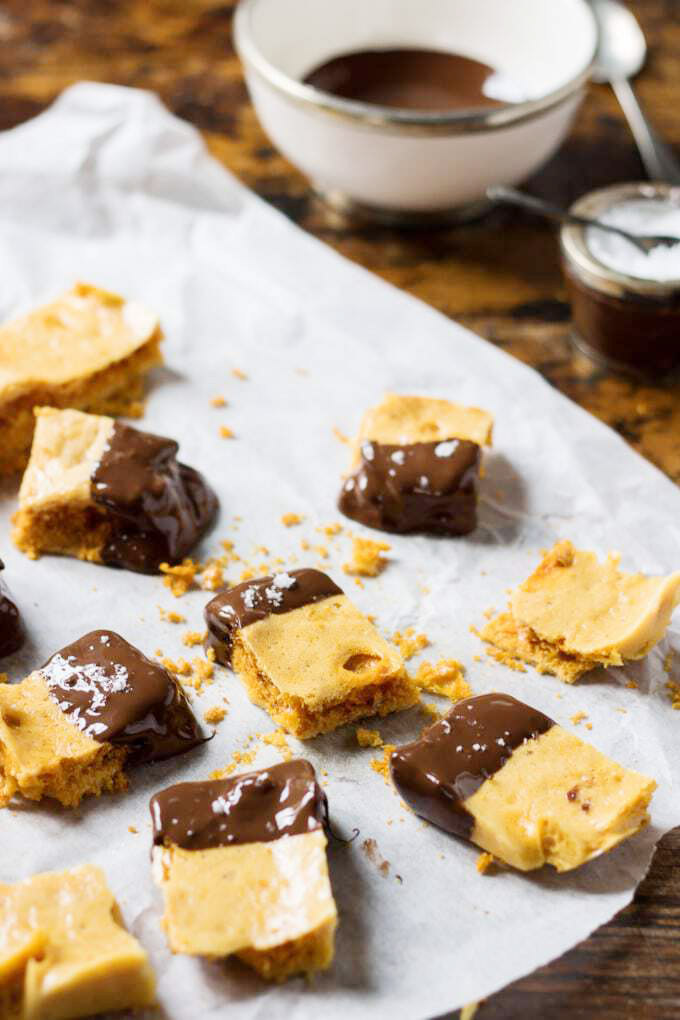 Pieces of chocolate honeycomb sitting on a parchment paper on a wooden table.