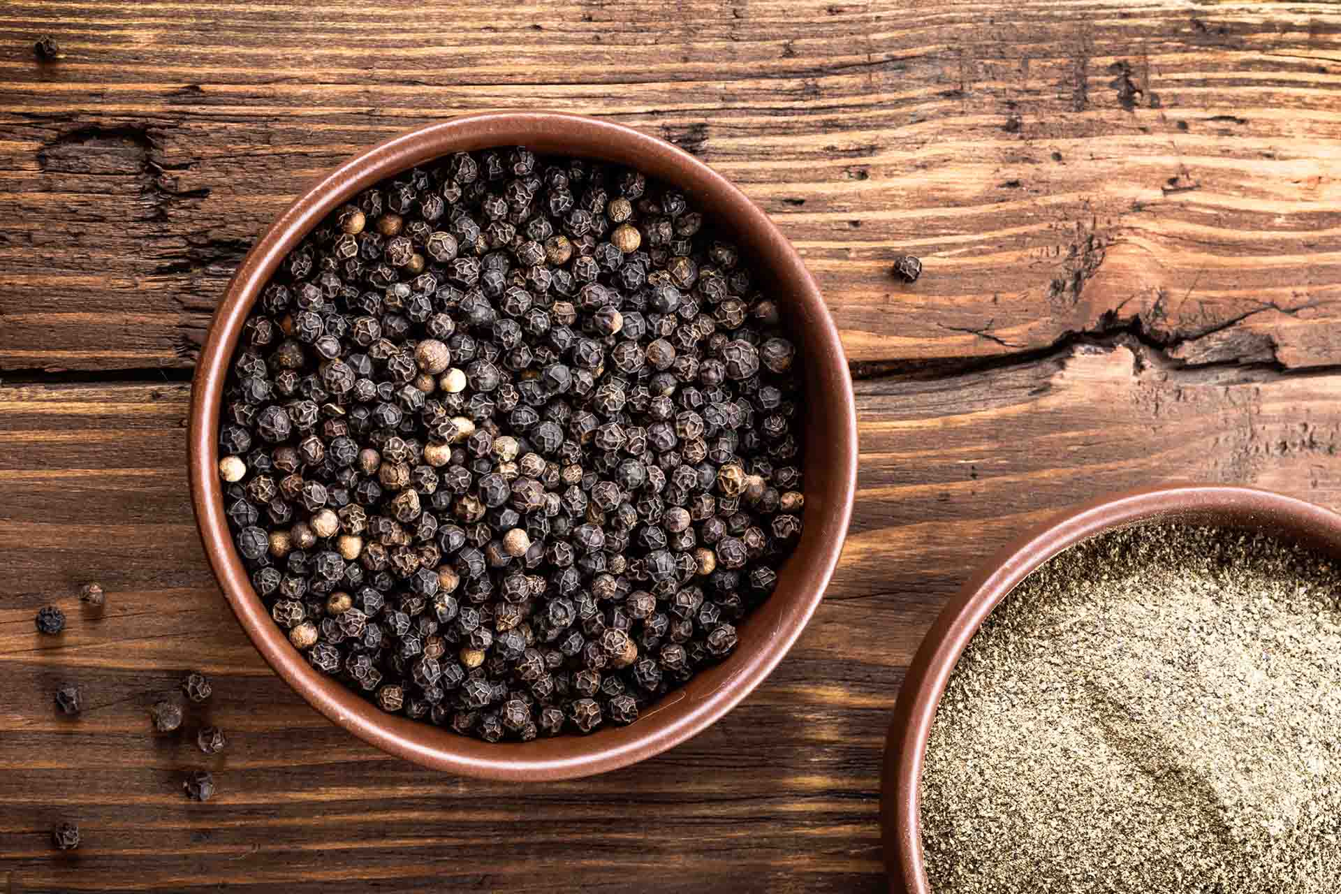 Bowl of black peppercorns sitting on a wooden table.