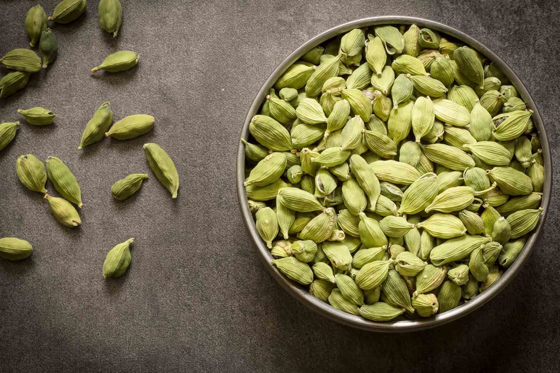 Green cardamom pods in steel bowl with wooden background.