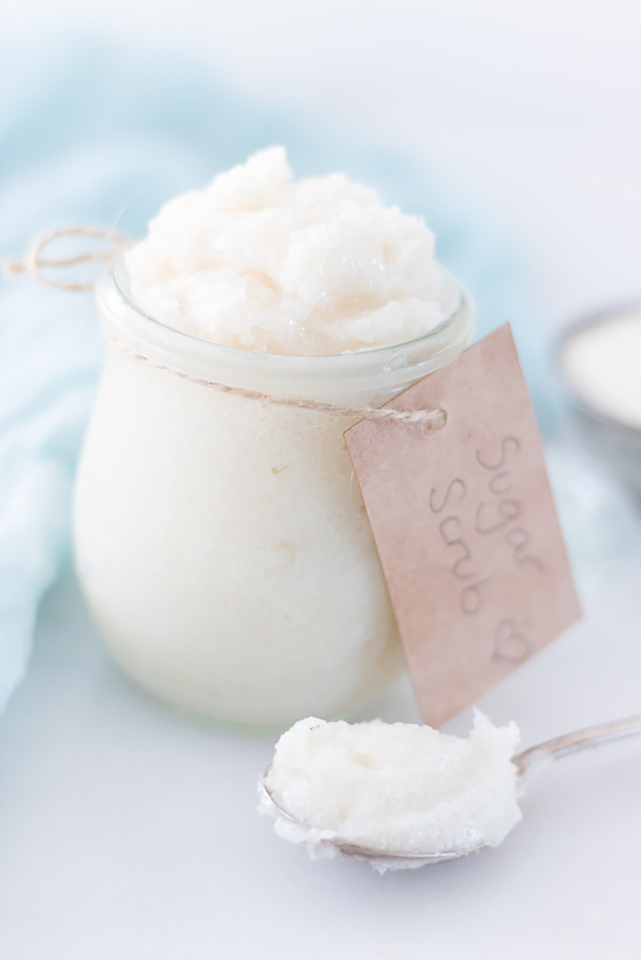 A jar of homemade sugar scrub with a tag sitting on a white counter.