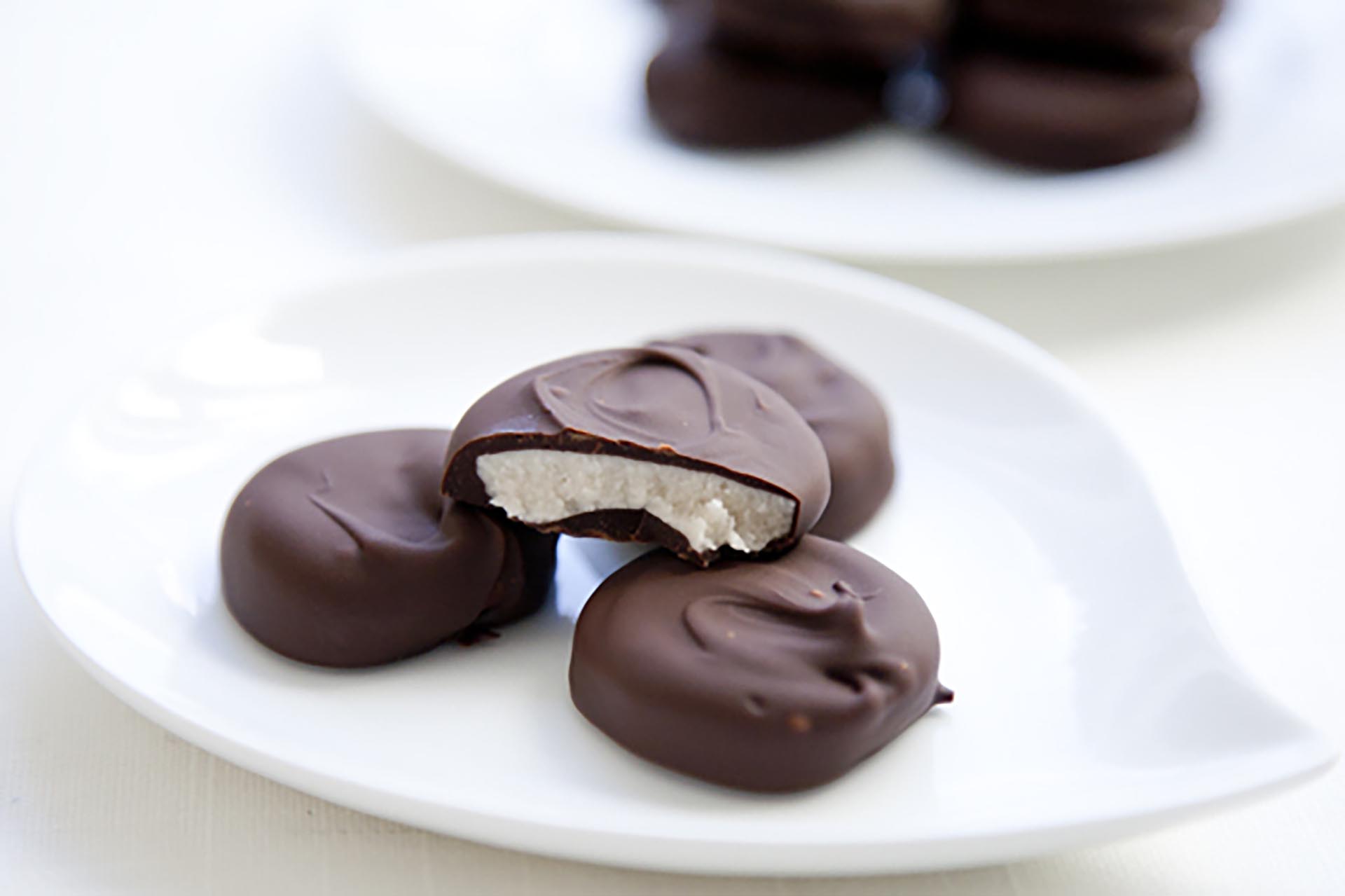 A white plate with a few peppermint patties sitting on a white table with another plate of peppermint patties in the background.