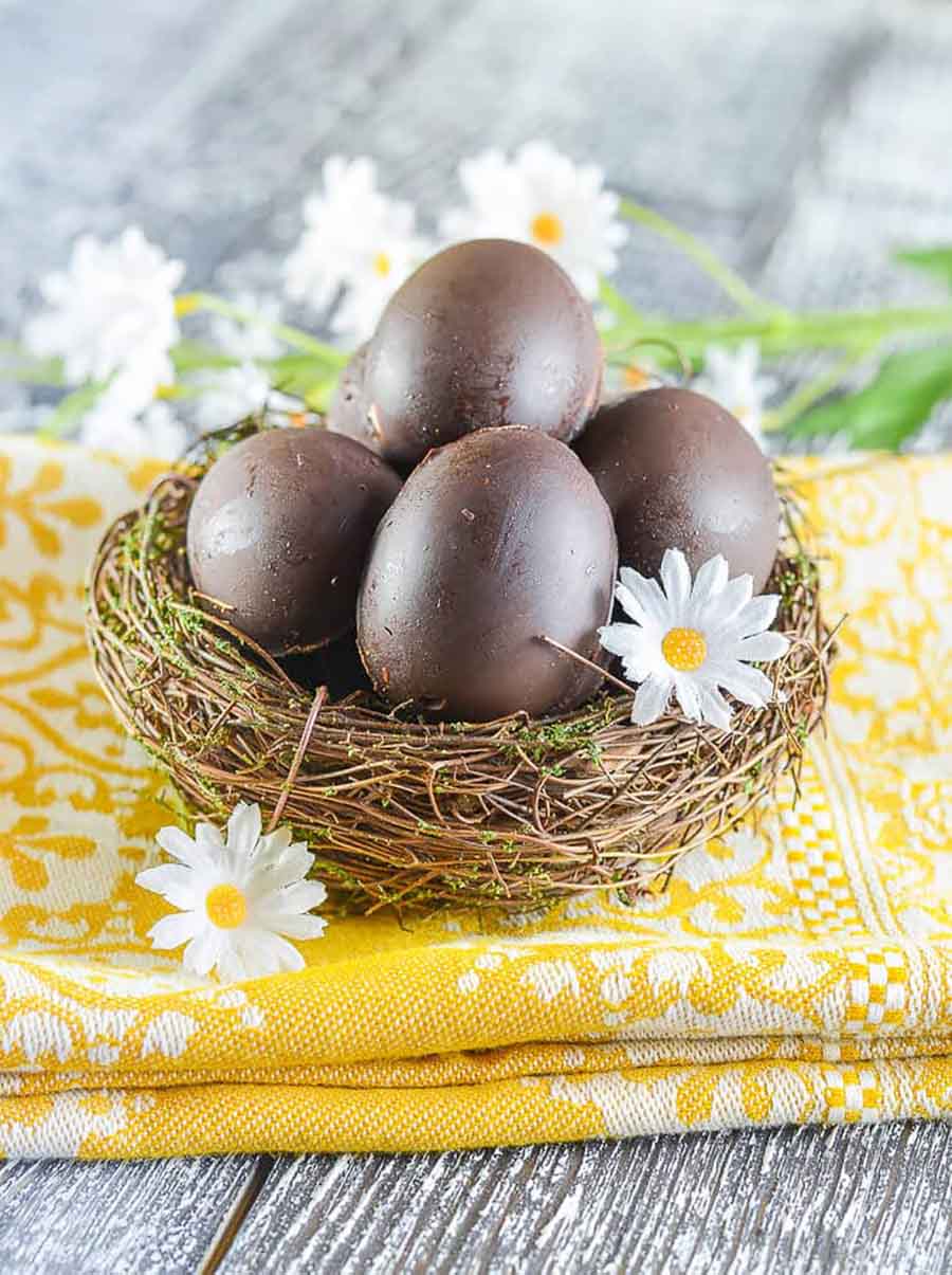 A wooden basket filled with chocolate creme eggs sitting on top of a yellow cloth napkin on top of a wooden table.