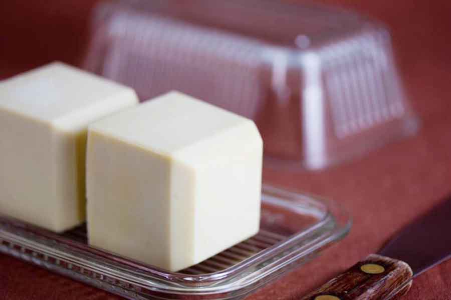 Two butter cubes sitting in a glass dish on a red table near a knife