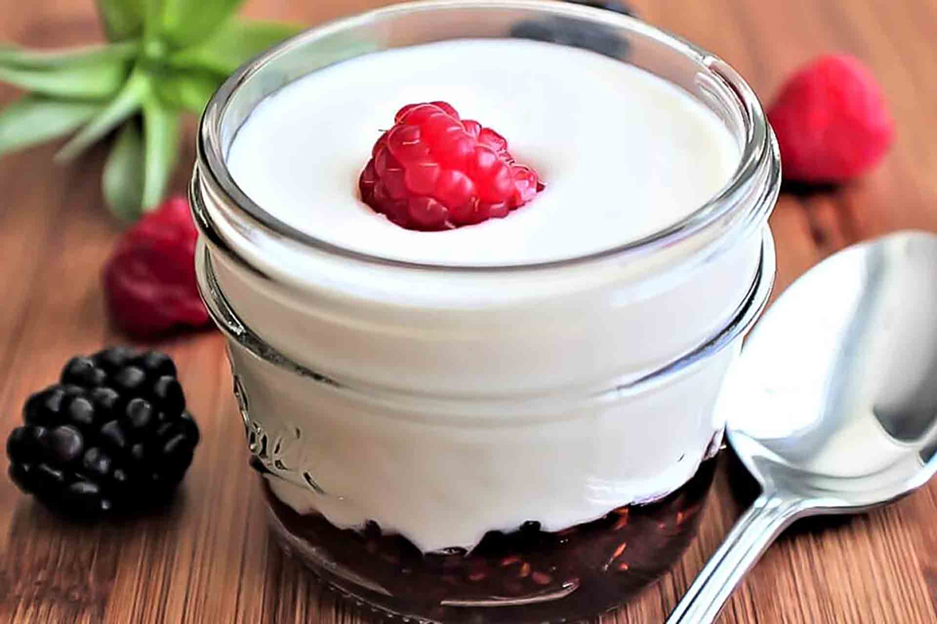 A glass jar of yogurt topped with a raspberry