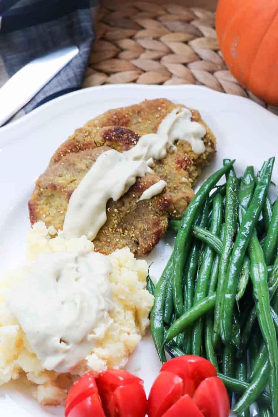 White plate filled with green beans, mashed potatoes, tomatoes, and seitan steaks