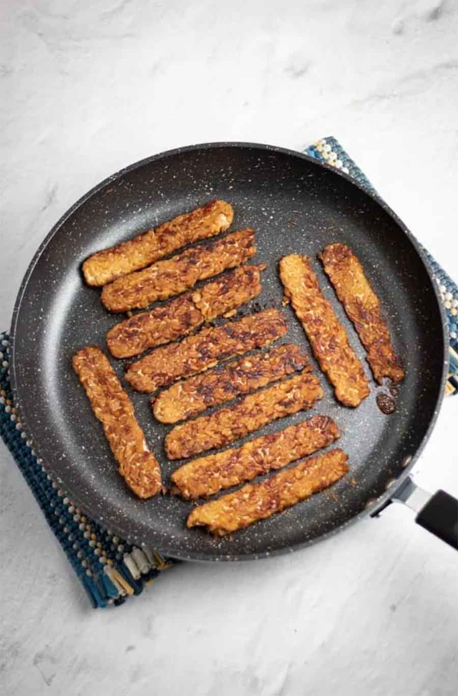 A black skillet with tempeh bacon sitting on a counter