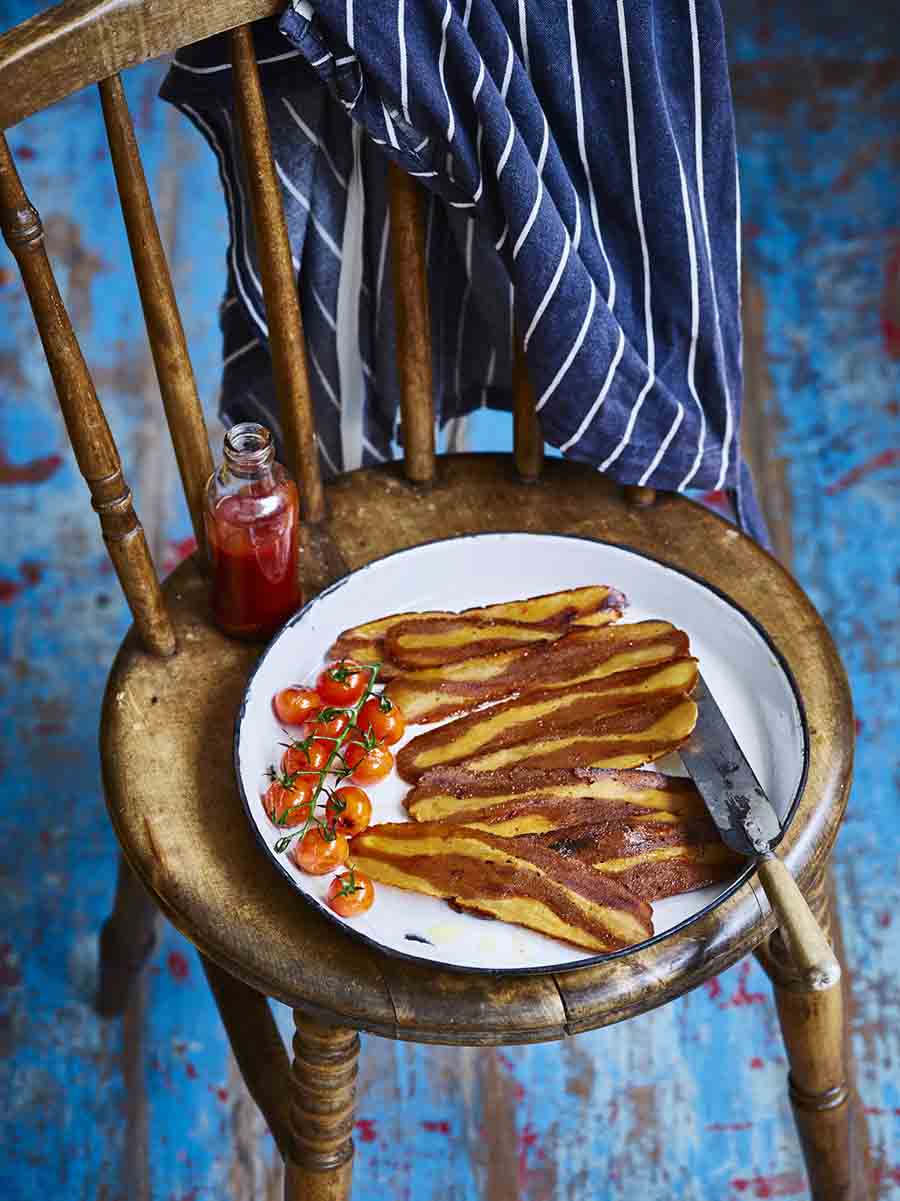 A white plate of bacon sitting on a wooden chair in a blue room
