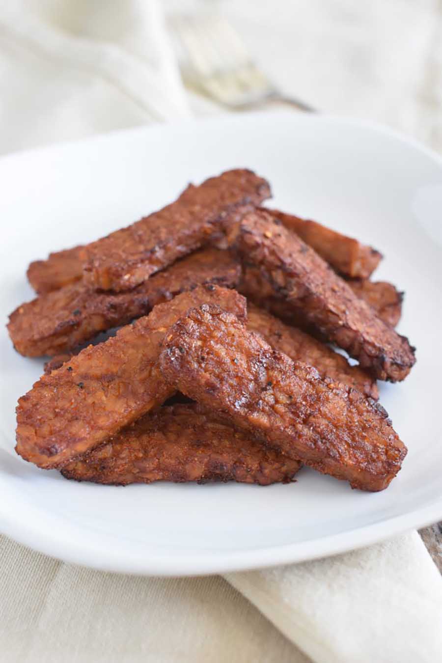 A white plate with piles of tempeh bacon sitting on a table